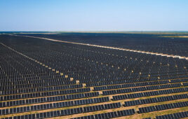 A large-scale solar project installed on arid land stretches to the horizon.