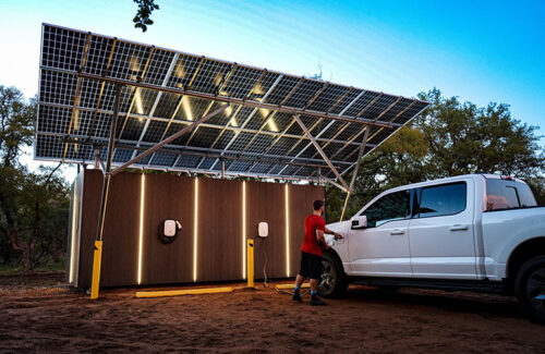A person is plugging an electric vehicle charger into a truck that is parked beneath a canopy of solar panels. 