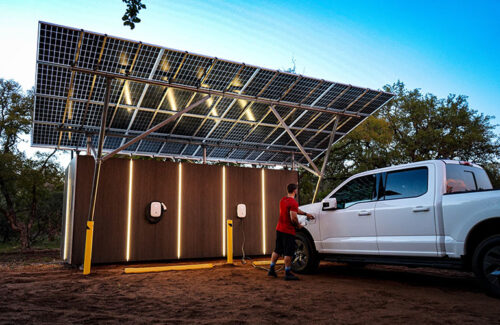 A person is plugging an electric vehicle charger into a truck that is parked beneath a canopy of solar panels.